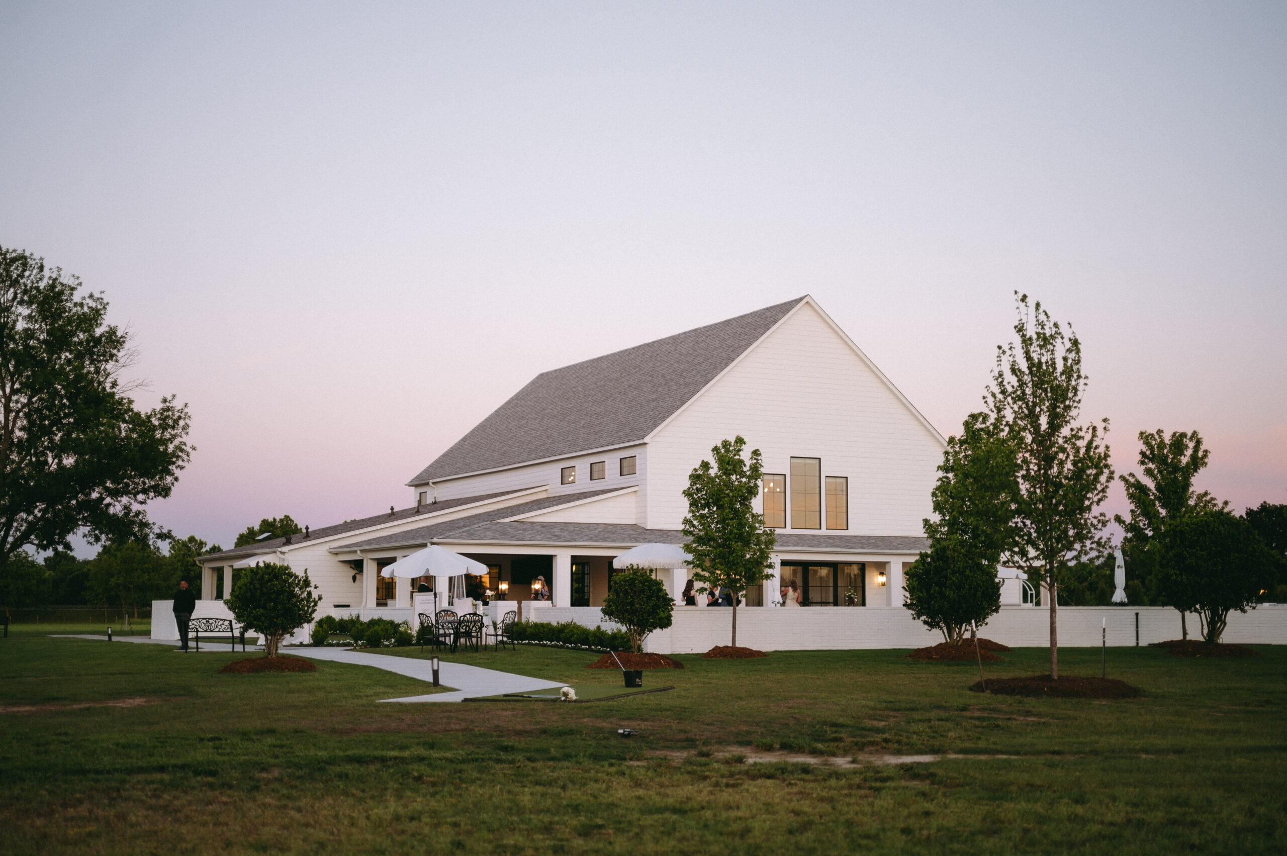 Sunset at Bluestem Manor featuring the large white reception hall, outdoor patio with umbrellas, and manicured lawn for outdoor wedding cocktail hours.