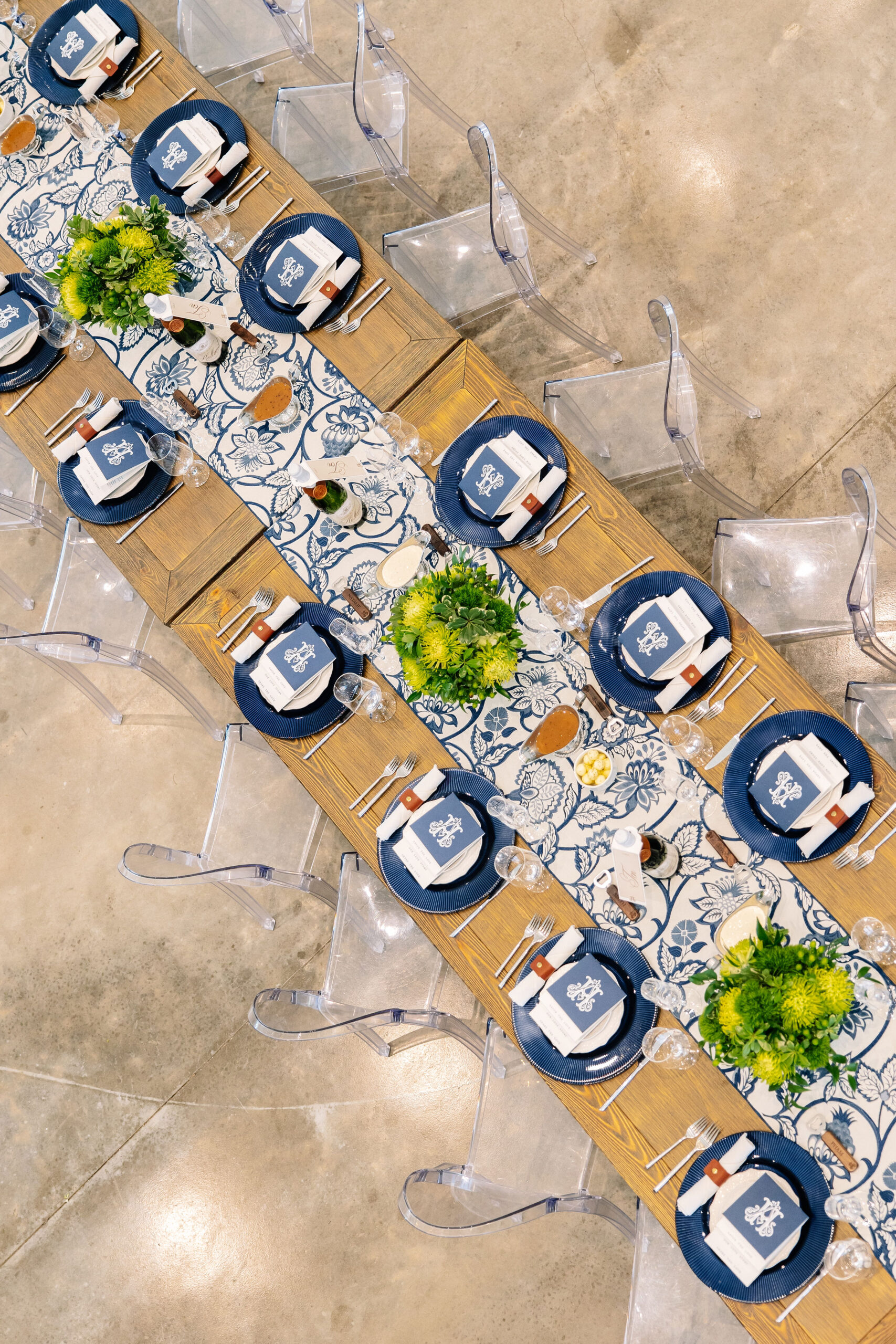 Bird’s eye view of a wedding reception table at Bluestem Manor, featuring a blue and white floral runner, navy chargers, and modern ghost chairs.